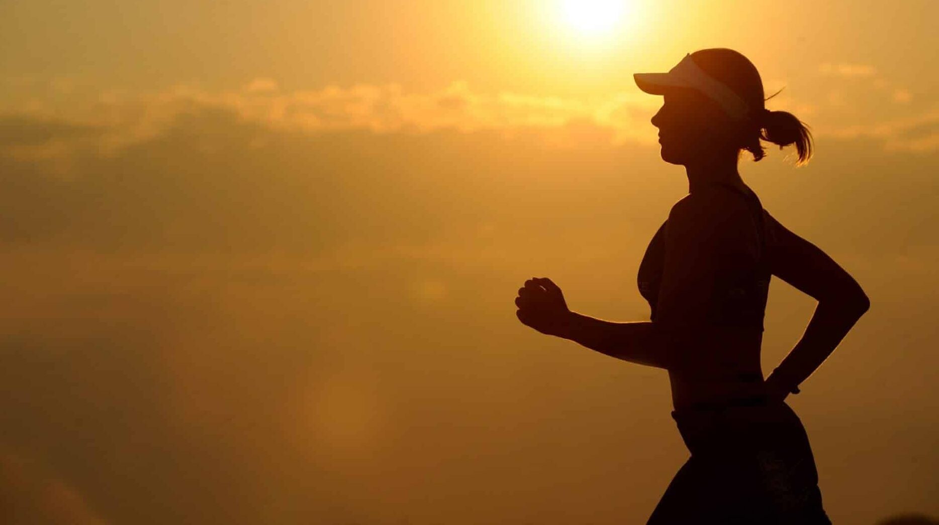 A woman wearing a hat, running with a sunset in the background.