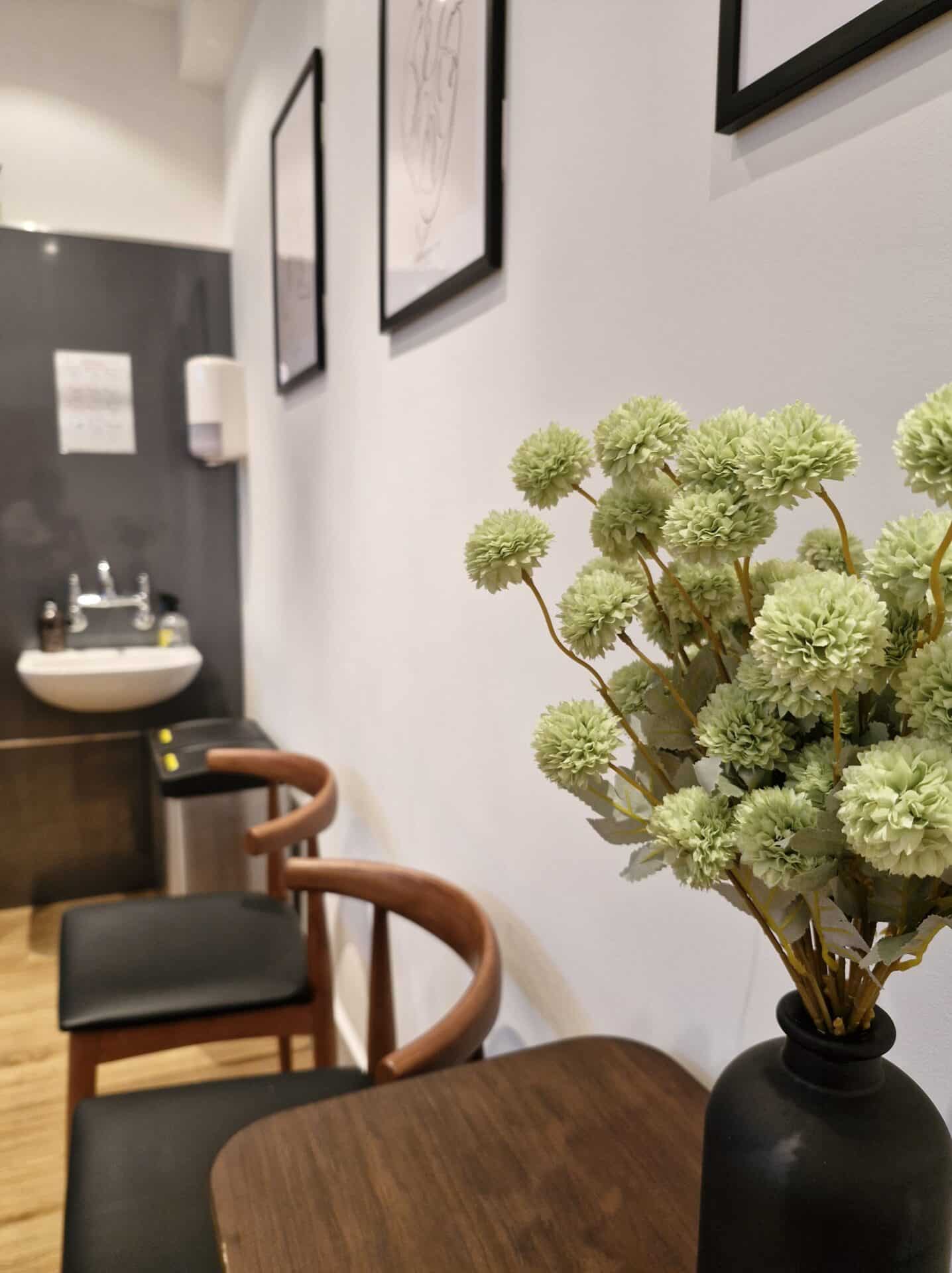 A close up of flowers in a vase on top of a sideboard with a sink in the background.